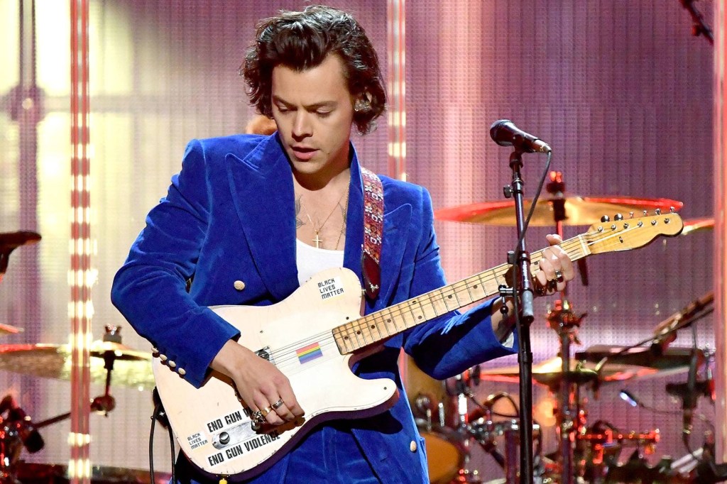 Harry Styles in a blue velvet suit with a guitar